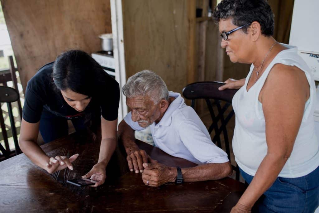 Elderly hispanic man experiencing memory loss looking at a phone screen with adult and teenage female relatives